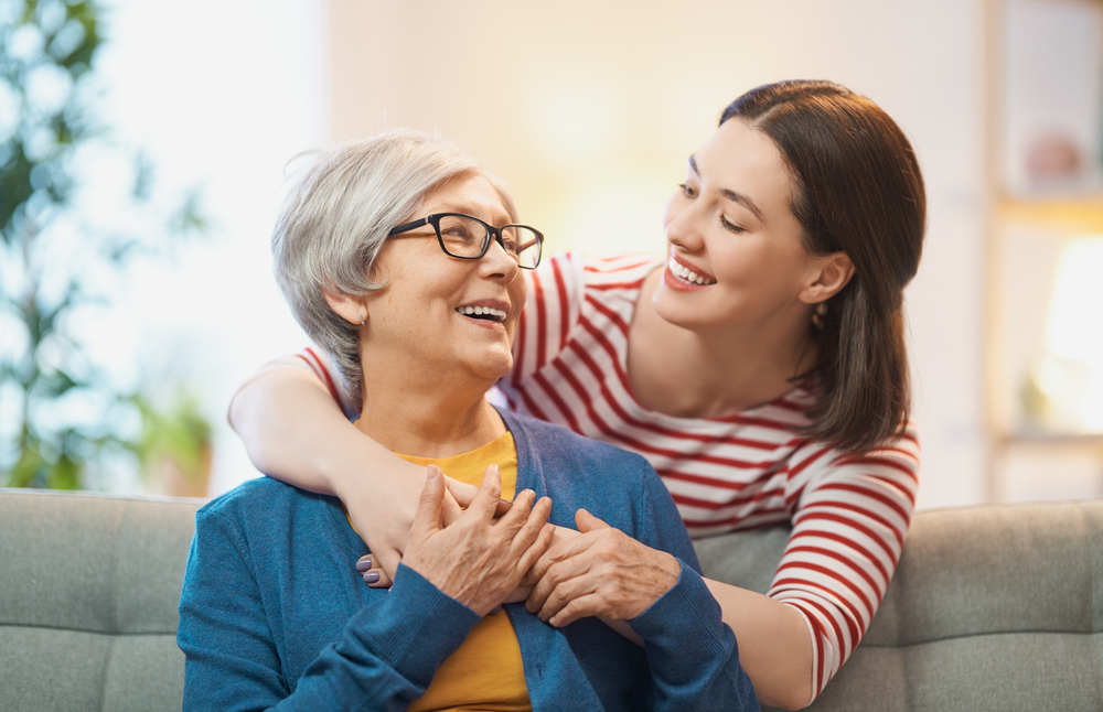 Elderly Woman and Young Woman Smiling Together - Mount Carmel Eye Doctor Happy elderly woman in glasses shares a warm moment with a younger woman in a red-and-white striped shirt, both smiling brightly - Mount Carmel Eye Doctor
