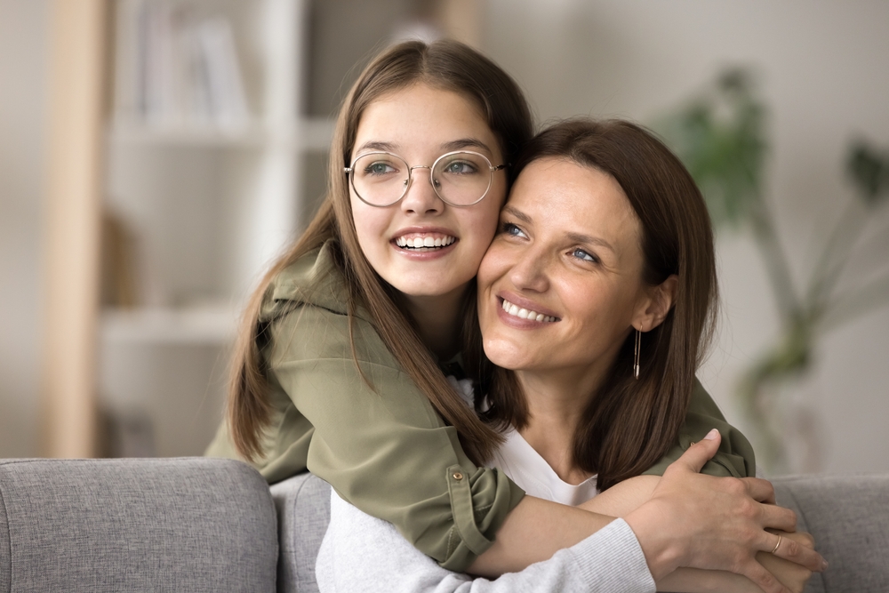 Mother and Daughter Smiling and Hugging - Eye Exam Kingsport TN Happy mother and daughter, both wearing glasses, share a warm hug while sitting together at home - Eye Exam Kingsport TN.