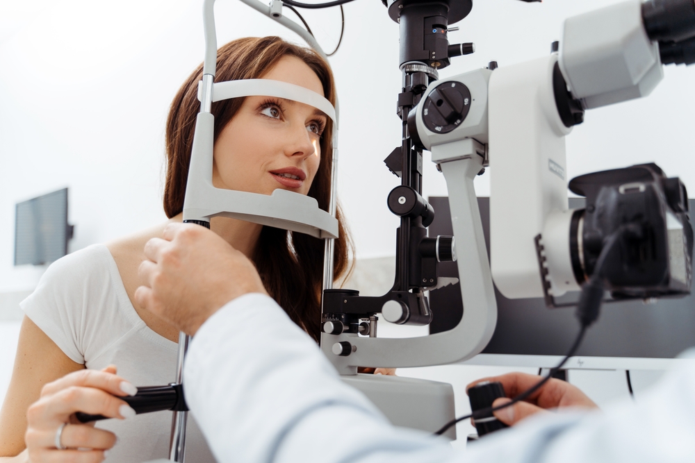 Woman Getting Eye Exam with Slit Lamp Machine A woman sits at an optometrist’s office undergoing an eye health check using a slit lamp examination device.