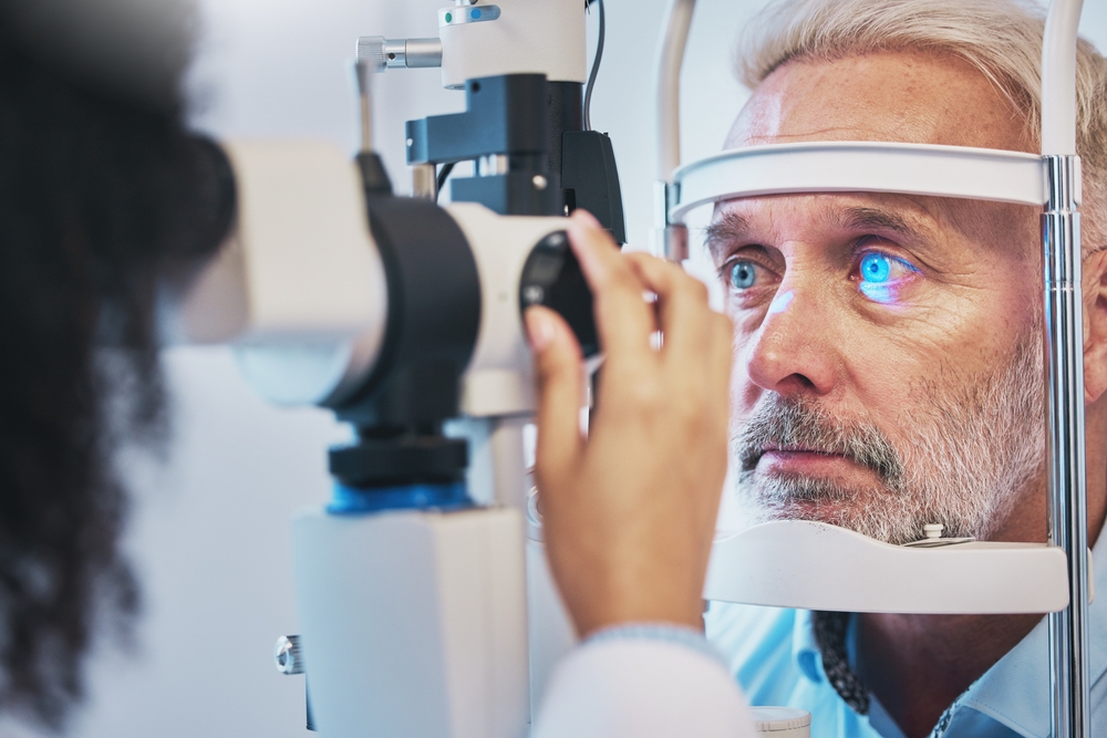 Senior Man Receiving Slit Lamp Eye Examination An older man with gray hair undergoes a slit lamp eye exam, with blue diagnostic light reflecting in his eye as the optometrist adjusts the equipment.